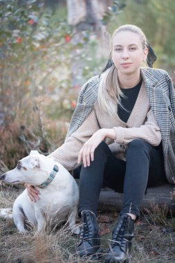 Genç ve çekici bir kadın sonbahar parkında köpekle oynuyor.