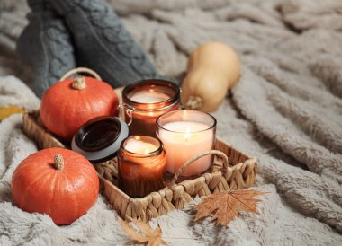 Süveter ve örgü çoraplı bir kız battaniyeye oturur. Sıcak sonbahar konsepti. Balkabakları ve mumlar kızın yanındaki tepside..