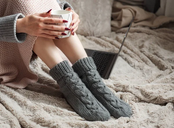 Cozy home, woman covered with warm blanket, drinks coffee and works on a laptop. Relax, carefree, comfort lifestyle.