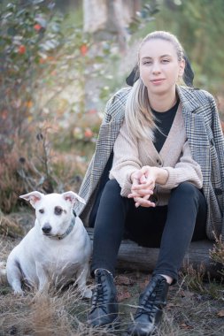 Genç ve çekici bir kadın sonbahar parkında köpekle oynuyor.