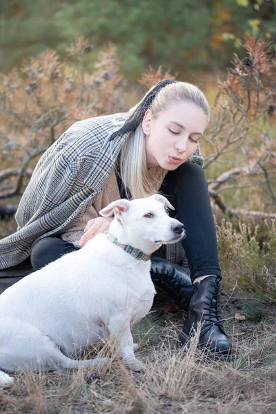 Genç ve çekici bir kadın sonbahar parkında köpekle oynuyor.