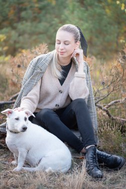 Genç ve çekici bir kadın sonbahar parkında köpekle oynuyor.