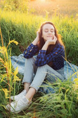 Portrait of a beautiful young woman on meadow watching the sunset enjoying nature summer evening outdoors.