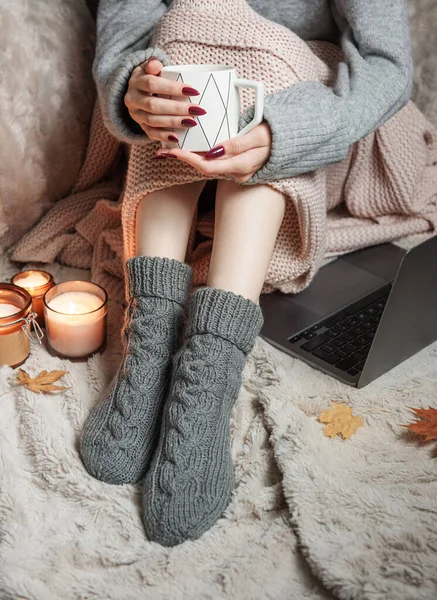 Cozy home, woman covered with warm blanket, drinks coffee and works on a laptop. Relax, carefree, comfort lifestyle.