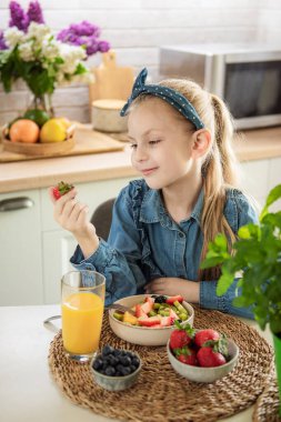Evde sağlıklı yiyecekler. Tatlı küçük kız meyve salatası yiyor. 