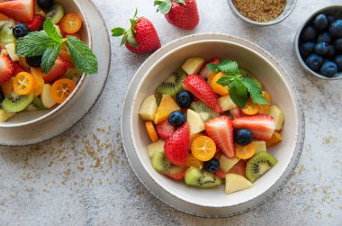 Beton arka planda bir kasede sağlıklı taze meyve salatası.
