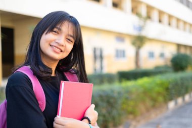 Öğrenci genç kız okulda pembe kitap ve sırt çantası tutuyor, okula geri dönüyor..