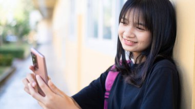 Okulda akıllı telefon kullanan güzel bir genç kız, Asyalı bir kız, turuncu bir geçmişi var..