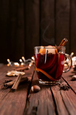 Noel zamanı konsept fotoğrafı. Cam bardak ya da kupa, içinde şarap olan ahşap masa ve arka plan. Çelenkler, süslemeler, tarçın, fındık, kurutulmuş ya da süblimleşmiş portakal, elma, çeşitli baharatlar.