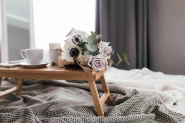 Romantik bir sabah. Yatağında çiçekler, ekose kahve fincanı, çiçekler ve mumlar olan ahşap sehpa. Okaliptüs ve şakayıklı leylak gülleri. İç gri tonlar. Yüksek kalite fotoğraf