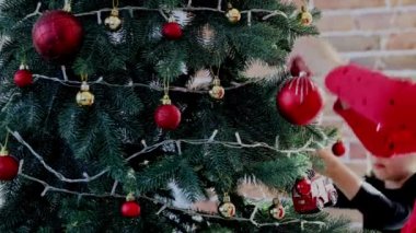 Çocuk elleri Noel ya da yılbaşı ağacını küre oyuncaklarıyla süsler. İki küçük kız kardeş dikkatle düzleştirip beyaz top koydular. Küçük kızlar Noel süslemesi takıyor Noel süslü köknar ağacına