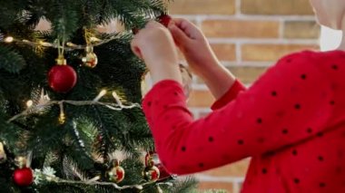 Çocuk elleri Noel ya da yılbaşı ağacını küre oyuncaklarıyla süsler. Çocuk dikkatlice doğrult ve beyaz topu at. Küçük kız Noel süslerini çelenk ışıklarıyla asar ve Noel ağacına asar.
