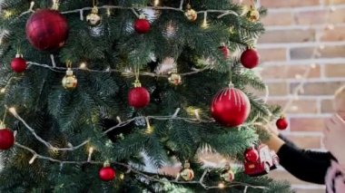 Çocuk elleri Noel ya da yılbaşı ağacını küre oyuncaklarıyla süsler. Çocuk dikkatle beyaz topu attı. İki küçük kız kardeş Noel süslerini süslenmiş çelenk ışıklarıyla süslüyorlar.