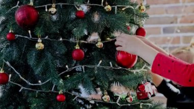 İki kız kardeş Noel 'i ya da Noel ağacını küre oyuncaklarıyla süslüyor. Çocuk dikkatlice doğrult ve beyaz topu at. Küçük kız ağaçlara ışıklarla Noel süsü asıyor.