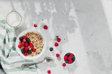 Kahvaltı kasesi granola, müsli, ahududu, böğürtlen ve gri masada.