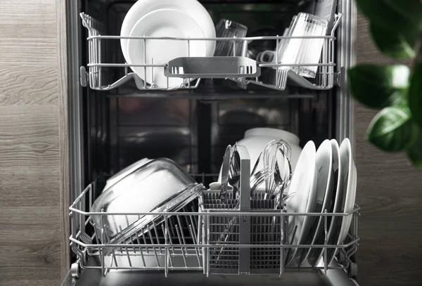 Відкрита посудомийна машина з чистим посудом всередині, столові прибори, окуляри, посуд на кухні — стокове фото