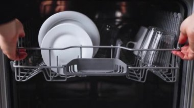 Kadın elleri bulaşık makinesi sepetini, açık makineden yıkanmış tabağı alır.