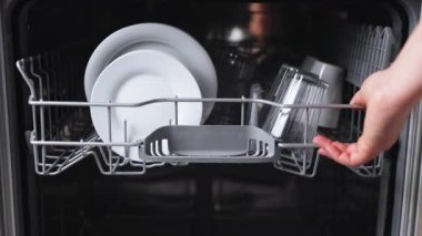 Kadın elleri bulaşık makinesinden çamaşır sepetini çıkarır, yıkanmış cam bardağı makineden alır.