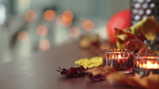 Hořící svíčky se žlutě zaschlými podzimními listy ležícími na dřevěném stole. Dýně a rozmazaná blikající světla na pozadí. Koncept Díkůvzdání na podzim. Vysoce kvalitní FullHD záběry