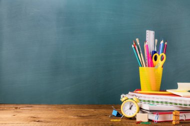 Birçok farklı okul, ofis malzemeleri ve kırtasiye malzemeleri. Okul konseptine geri dönelim. Defter, kitap, kalem, makas, çalar saat, saat, saat yeşil arka plandaki ahşap bir masanın üzerindeki çıkartma standı..