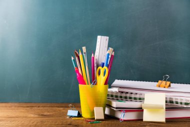 Birçok farklı okul, ofis malzemeleri ve kırtasiye malzemeleri. Okul konseptine geri dönelim. Defter, kitap, kalem, makas, çalar saat, saat, saat yeşil arka plandaki ahşap bir masanın üzerindeki çıkartma standı..