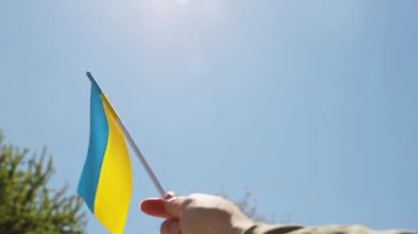 Ukraine national flag in human hand waving by wind in front of clear sky, sun. Small blue-yellow symbol souvenir of nation, freedom, nationality, strength, will and honor. High quality FullHD footage