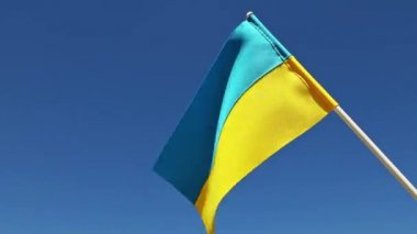 Ukraine national flag in human hand waving by wind in front of clear blue sky. Small blue-yellow symbol souvenir of nation, freedom, nationality, strength, will and honor. High quality FullHD footage
