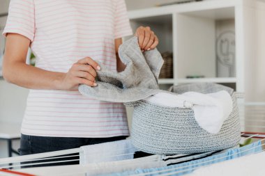 Woman boring, hanging clean wet clothes laundry on drying rack at home. Detail of female housewife hands closeup holding, spreading and taking laundry basket in front of clothing rack dryer