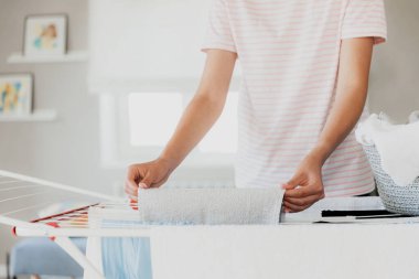 Woman hanging clean wet clothes laundry on drying rack at home in room. Detail of female housewife hands closeup hanging laundry on clothing rack dryer. Household chores. The woman puts the towel