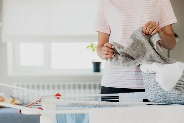 Woman hanging clean wet clothes laundry on drying rack at home in room. Female housewife hands closeup holding, spreading laundry from basket. Household chores. Girl holds folded bath towels in hand