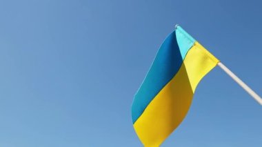 Ukraine national flag in human hand waving by wind in front of clear blue sky. Small blue-yellow symbol souvenir of nation, freedom, nationality, strength, will and honor. High quality FullHD footage