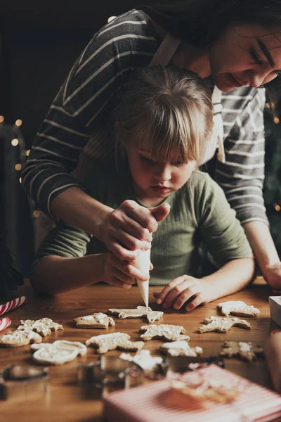Christmas and New Year food preparation. Xmas gingerbread cooking, making and decorating freshly baked cookies with icing and mastic. Mommy and child, authentic lovely moments. DIY, creativity concept