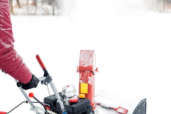 Closeup of portable red snow blower powered by gasoline in action. Man outdoor using snowblower machine after snowstorm for clearing, removing snow on snowy road. Snow removal, thrower assistant