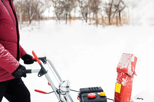 Detail of portable red snow blower powered by gasoline in action. Man outdoor using snowblower machine after snowstorm. Snow removal, thrower assistant in winter. Guy blowing snow during blizzard