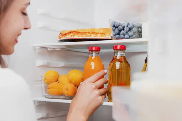 Kadın el ele tutuşuyor, meyve suyu şişesini açık buzdolabından alıyor ya da meyve, sebze, muz, şeftali ve yoğurt dolu buzdolabı çekmecesinden alıyor. Sağlıklı beslenme, yaşam tarzı konsepti