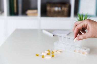 Hapları düzenleyen, sıralayan yaşlı kadın elleri. Günlük haplarla dolu ilaç kutusu beyaz, sarı, bej, kapsüllü. Genç kadın günlük vitaminlerini evde alıyor.