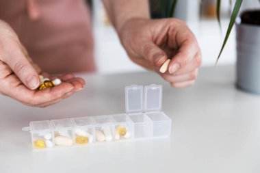 Kadın eli hapları ayırıyor. Genç bir kadın günlük vitaminlerini evde alıyor. İlaç kutusunun kapanışı, günlük dozda hap içeren beyaz, sarı haplar ve kapsüller içeren bir ilaç.