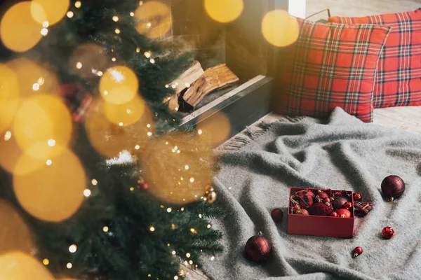 灰色のカーペットの上に寝そべっているクリスマスボールの箱や 照明付きの緑のクリスマスモミの木を飾ると吊るすために使用する準備ができているプレイ 内部の木材と暖炉の近くのリビングルームのガーランド — ストック写真