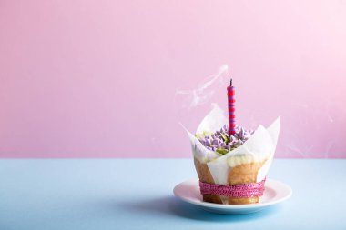 Çiçekli kek, üzerinde tek mum olan pembe arka planda mavi masa. Tereyağlı leylak çiçeğiyle süslenmiş güzel sünger fincan kekleri. Boşluğu kopyala.