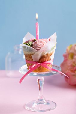 Mavi arka planda pembe masanın üzerinde tek mumlu çiçek keki. Tereyağlı güllerle süslenmiş güzel sünger fincan kekleri. Boşluğu kopyala.