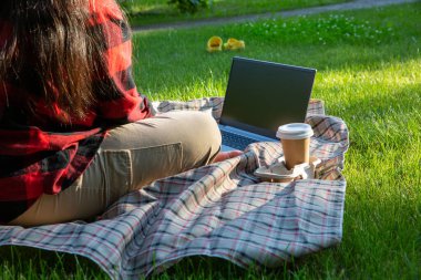 Bahçedeki çimlerin üzerinde dizüstü bilgisayarı ve bir fincan kahvesi olan bir iş yeri. Evden, serbest veya uzaktan çalışma kavramından çalışmak.  
