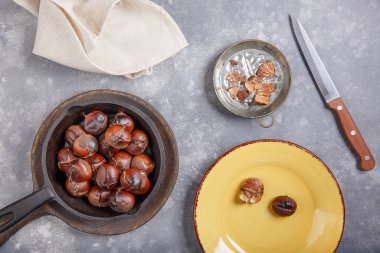 Gri arka plandaki dökme demir tavada servis edilen yenilebilir tatlı kestaneler. Üst görünüm.