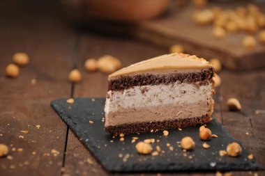 Üzerinde süslemeler olan, koyu arkaplanda servis edilen lezzetli çikolatalı pastanın bir parçası.