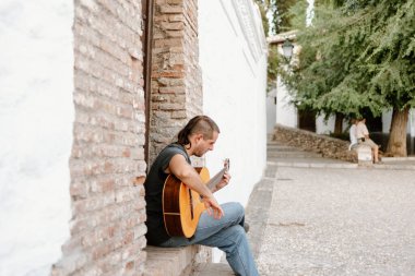 Granada, İspanya; 16 Ağustos 2017: Albaicin, Granada 'nın ünlü mahallesinde genç bir adam sokakta gitar çalıyor..