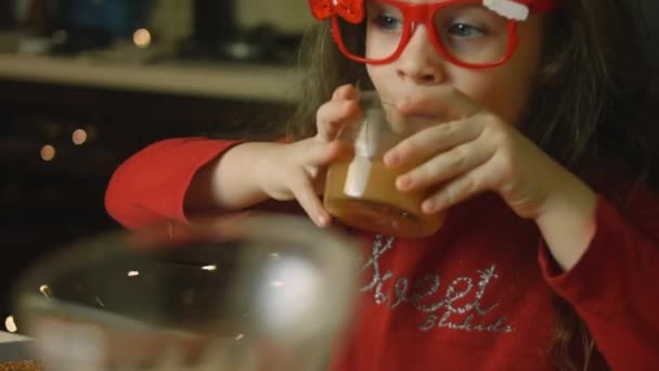 The little girl drinks a glass of juice while her mother prepares food — Stock Video