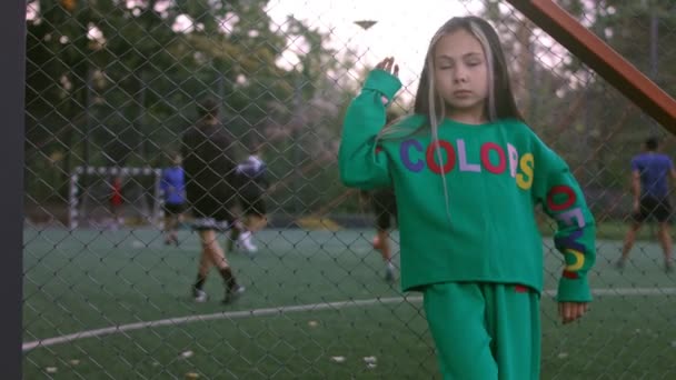 Das kleine Mädchen ist ein professionelles Model, das posiert. Fußballplatz im Hintergrund — Stockvideo