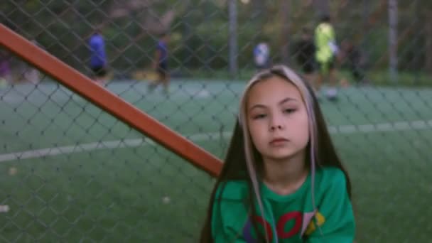 Das kleine Mädchen ist ein professionelles Model, das posiert. Fußballplatz im Hintergrund — Stockvideo