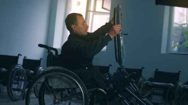 車椅子を作る工場でのワークショップでのアメリカ人男性労働者の1人の側面図、ハンドツールを使用して作業台に座って製品の一部を組み立てる、車椅子に座って — ストック動画