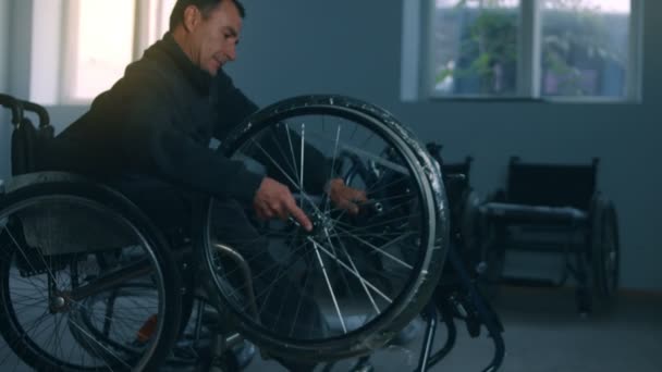 Side view of one American male workers in a workshop at a factory making wheelchairs, sitting at a workbench using hand tools and assembling parts of a product, sitting in wheelchairs — Stock Video