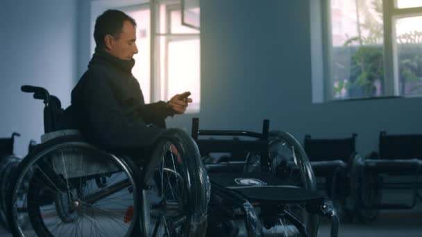 Vue latérale d'un travailleur américain dans un atelier d'une usine fabriquant des fauteuils roulants, assis sur un établi à l'aide d'outils à main et assemblant des pièces d'un produit, assis en fauteuil roulant — Video